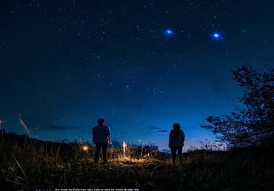 夜晚户外草坪上佩戴耳机的年轻人仰望星空，蓝色夜幕与点点繁星构成夜无疆音乐沉浸体验的意境画面